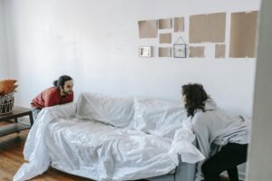 A couple rearranging furniture in their new apartment, lifting a wrapped couch together.